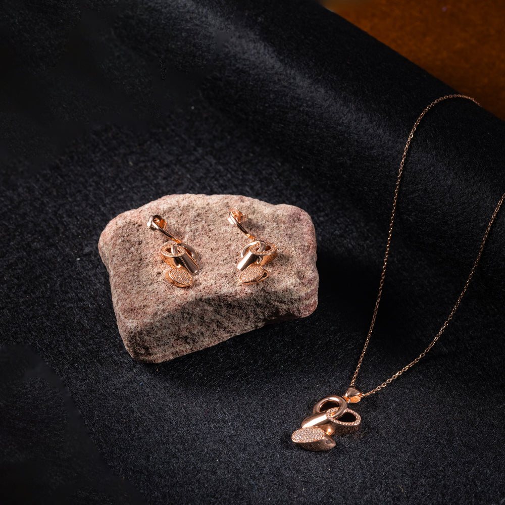Rose gold jewelry set including earrings and a necklace on a dark fabric background